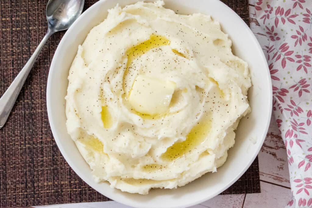 Overhead shot of finished Instant Pot Mashed Potatoes in a white bowl topped with butter and pepper 