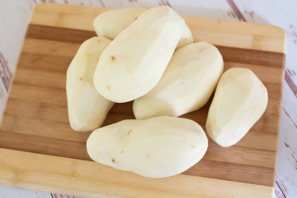 6 large peeled and washed potatoes on a cutting board 