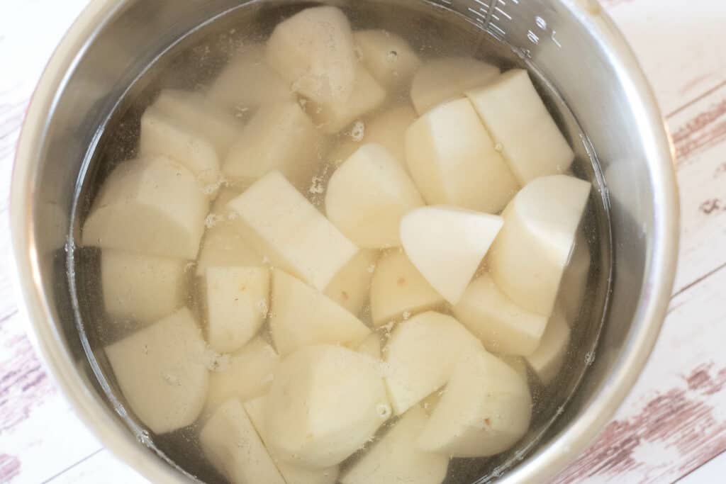 Chopped potatoes in the pot of an Instant Pot covered with water on a distressed wood surface 