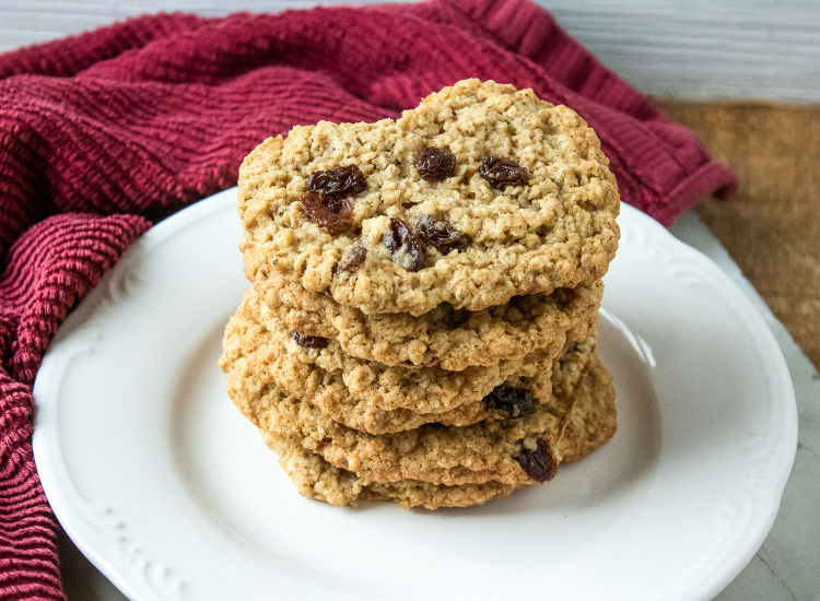 A stack of 6 oatmeal raisin cookies on a white plate with a red dish towel in the background 