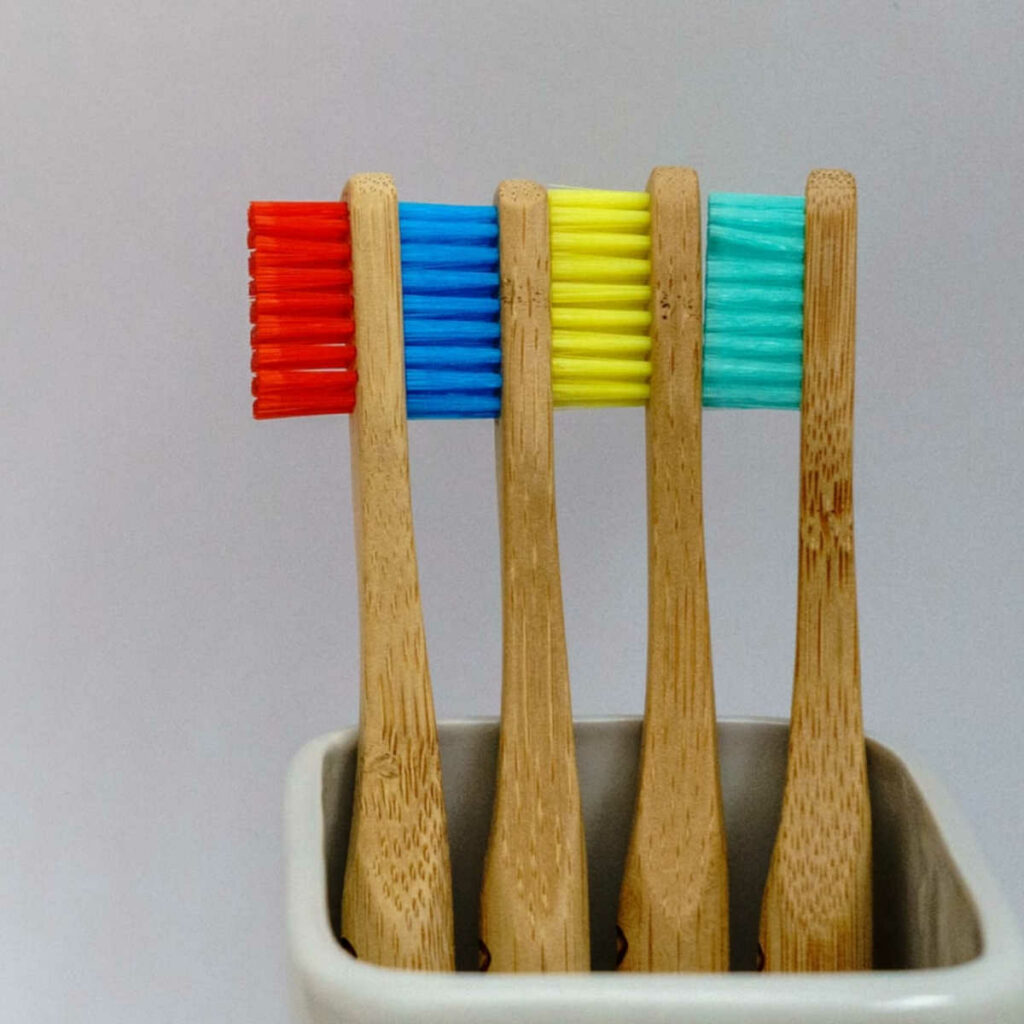 A square white container holding 4 toothbrushes with wooden handles and multicolored bristles