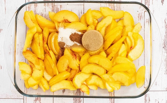Sliced peaches in a pan with sugar and spices on top. 