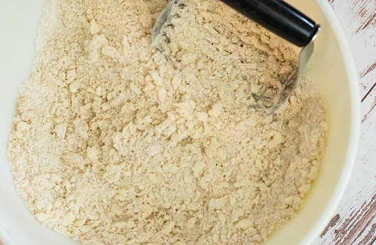 flour, sugar and butter mixed into a crumbly texture in a bowl with a pastry blender 