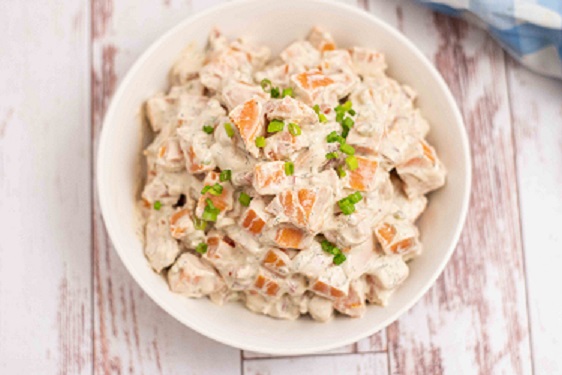 sweet potato salad garnished with green onions on a distressed white wooden table 