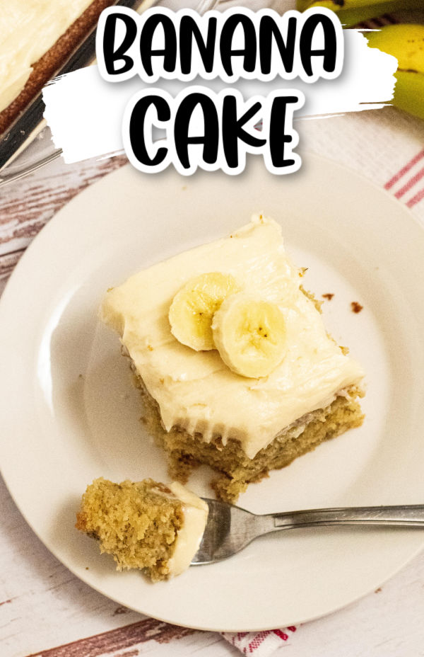 banana cake on a white plate with cream cheese icing and sliced banana on top with a bite taken out 