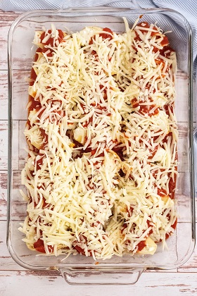 a 13x9 inch glass pan with stuffed shells covered with shredded mozzarella cheese 