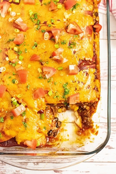 A glass pan of enchilada casserole with a piece cut out 