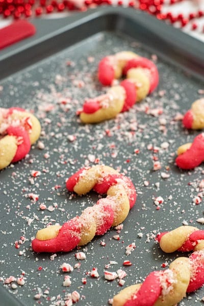 Candy cane cookies on a cookie sheet sprinkled with crushed peppermint. 