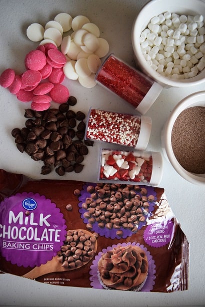 Ingredients for hot cocoa bombs, chocolate chips, hot chocolate mix, marshmallows, Valentine's Day sprinkles, white and pink chocolate melts 