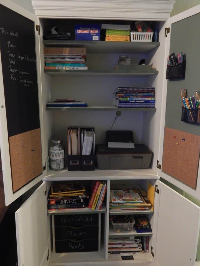 An open cabinet fll of homeschool supplies, books, paper, printer etc. 