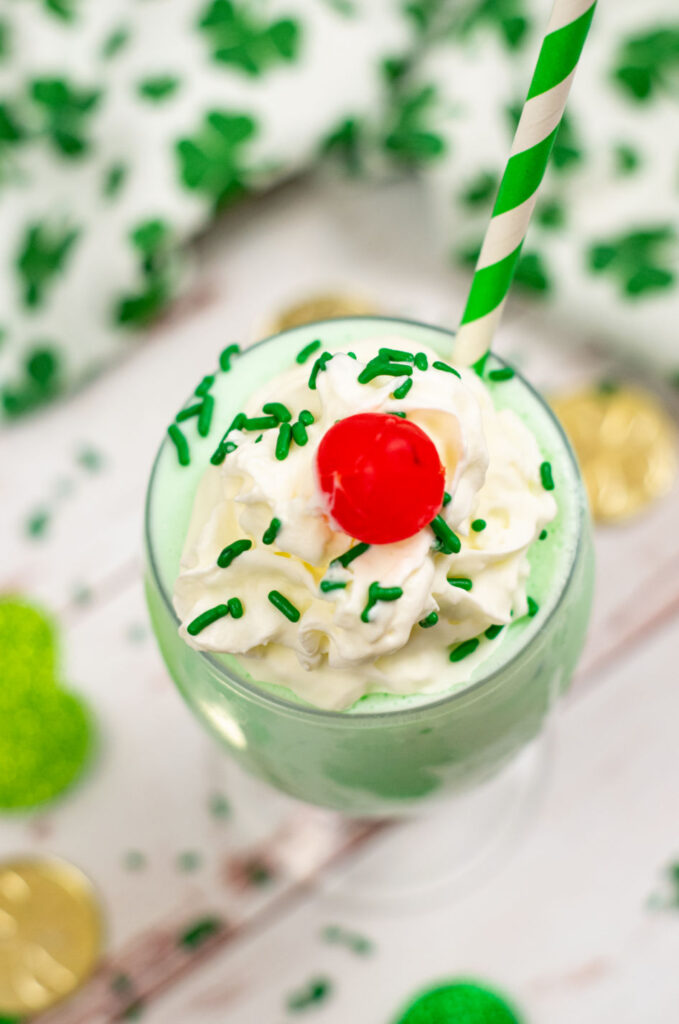 A keto shamrock shake topped with whipped cream in a cherry with a green and white striped straw