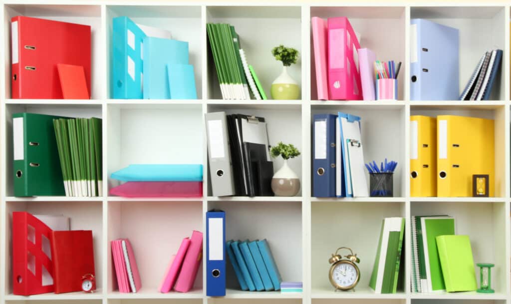 a set of cubical shelves with books and binders sorted in rainbow colors 