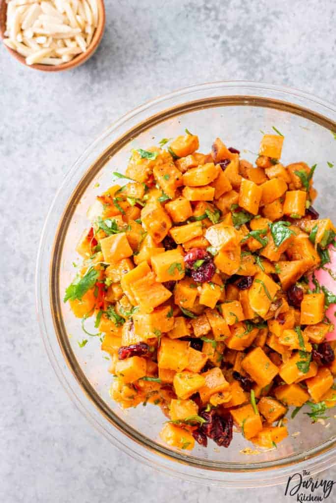A glass bowl full of cubed sweet potatoes, green garnish and dried cranberries