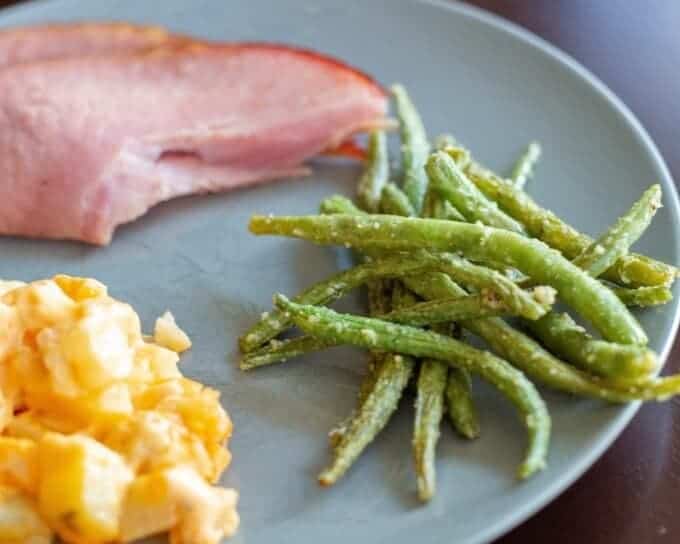 A blue plate with green beans, ham and cheesy potatoes
