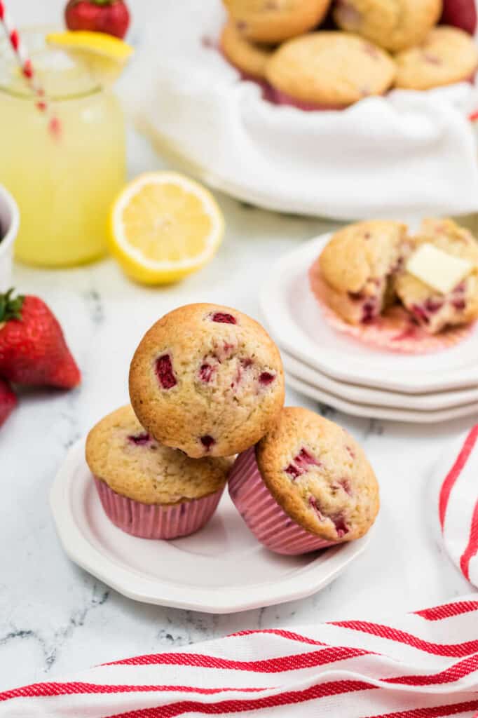 Strawberry lemonade muffins on a white plate. There are more muffins and  a glass of lemonade in the background 