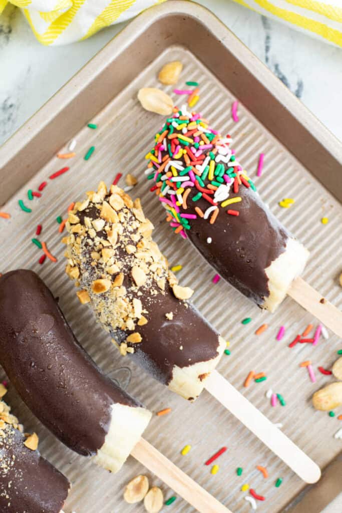 A close up of chocolate covered banana popsicles on a tray 