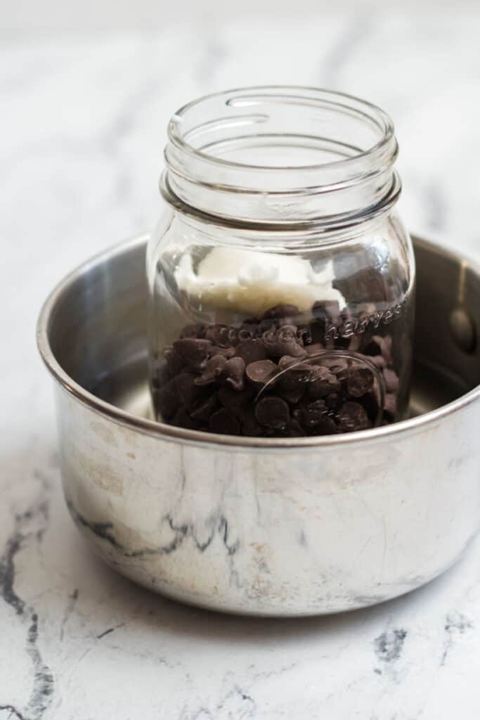 A mason jar full of chocolate chips and shortening in a small metal pan 
