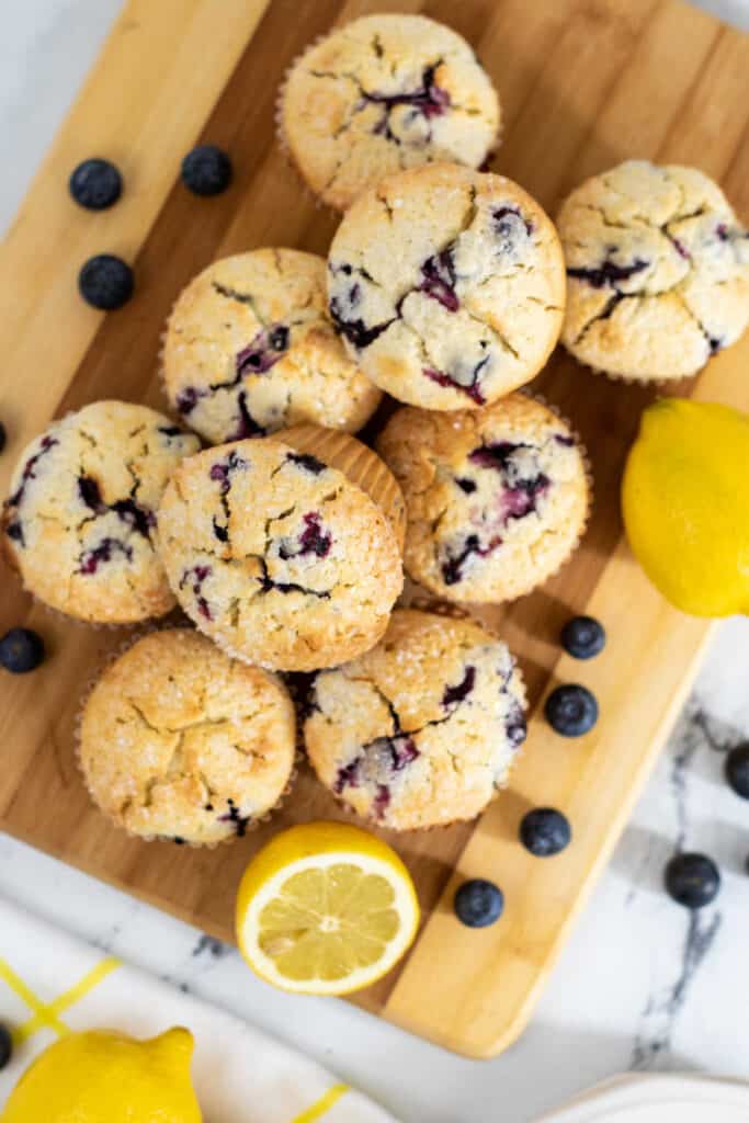 A wooden board with a pile of muffins on it with lemons and blueberries. 