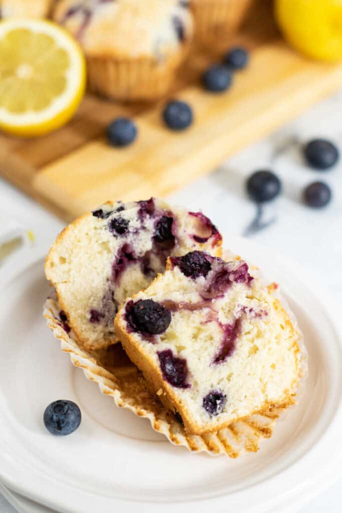 a lemon blueberry muffin cut in half on a white plate 