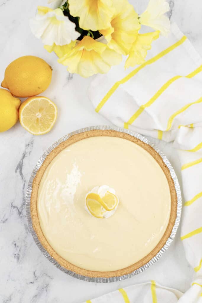 A lemon pie surrounded by a yellow and white linen and lemons 