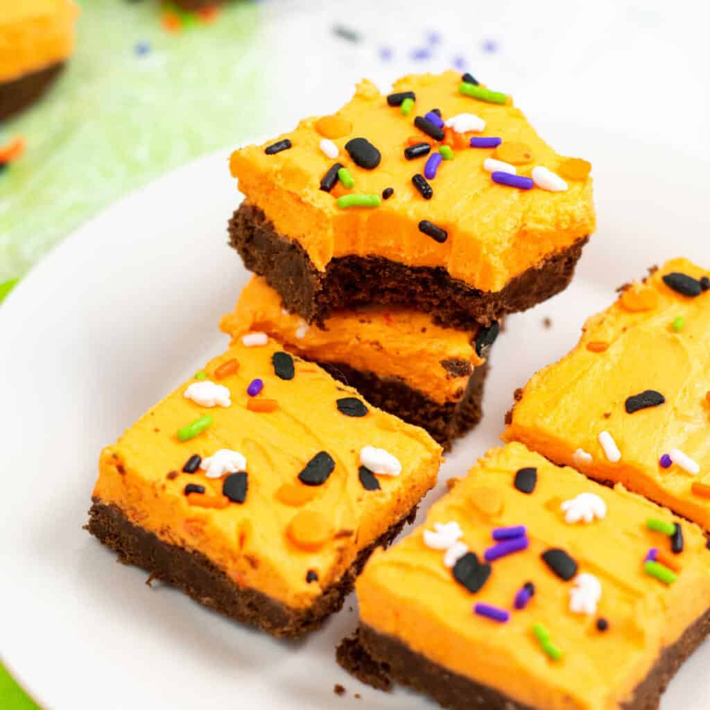 Chocolate cookie bars with orange frosting on a white plate 