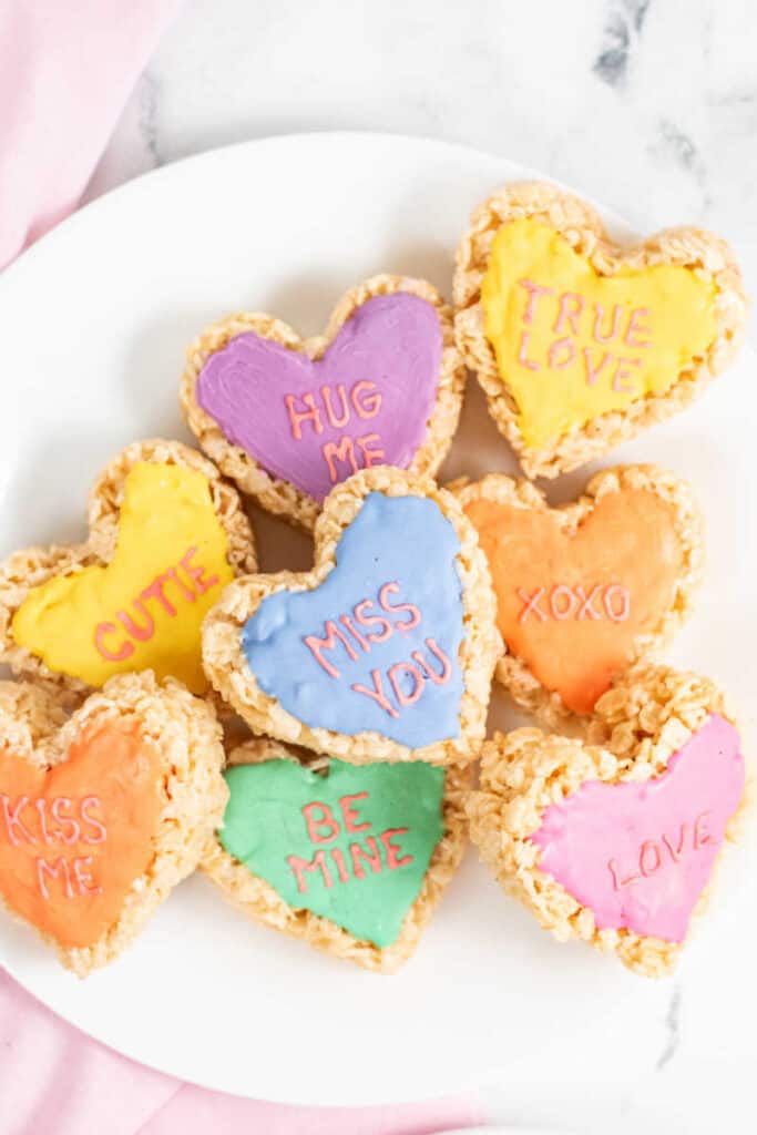 A plate full of colorful heart shaped rice krispie treats that have sayings on them. 