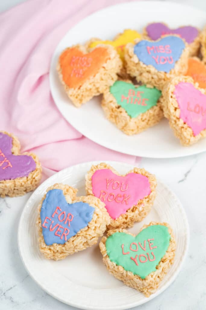 A large plate of conversation heart rice krispie treats with a smaller plate in front. 