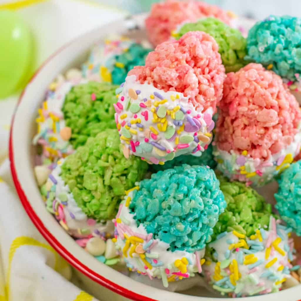 A bowl full of colorful eggs made with rice cereal treats. They have been dipped in white chocolate and covered with sprinkles. 
