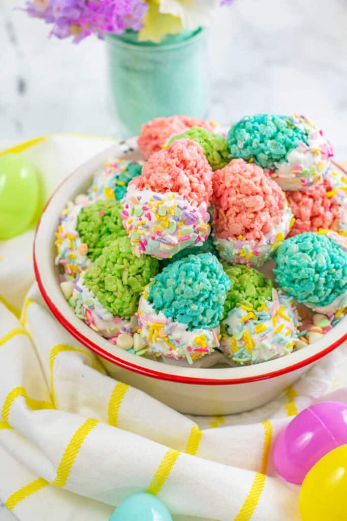 A bowl full of colorful rice krispie Easter eggs that have been dipped in white chocolate and coated with colorful sprinkles. 