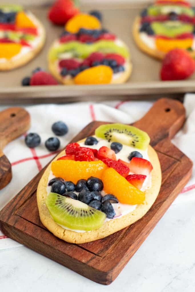 An egg shaped sugar cookie decorated with white frosting and chopped fruit and berries on a wooden plate. 