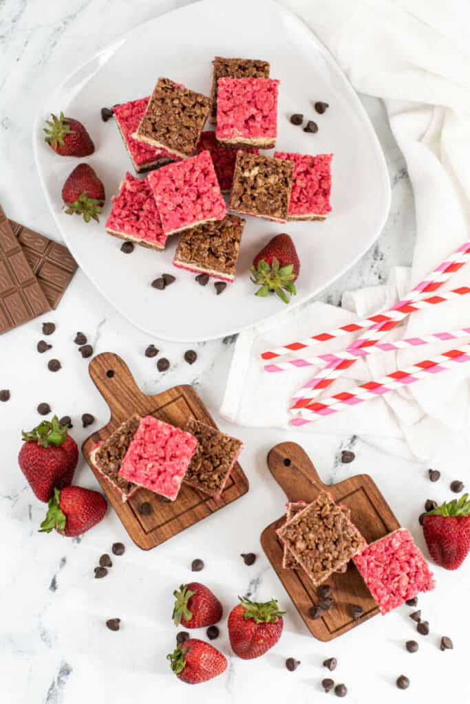 A table with a plate of Neapolitan rice krispies treats, around it sits chocolate bars and strawberries. 