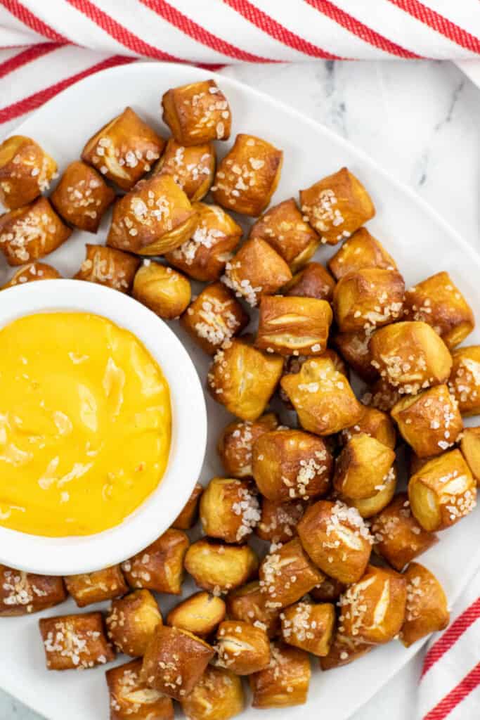 A white plate full of soft pretzel bites surrounding a small white bowl full of cheese dip. 