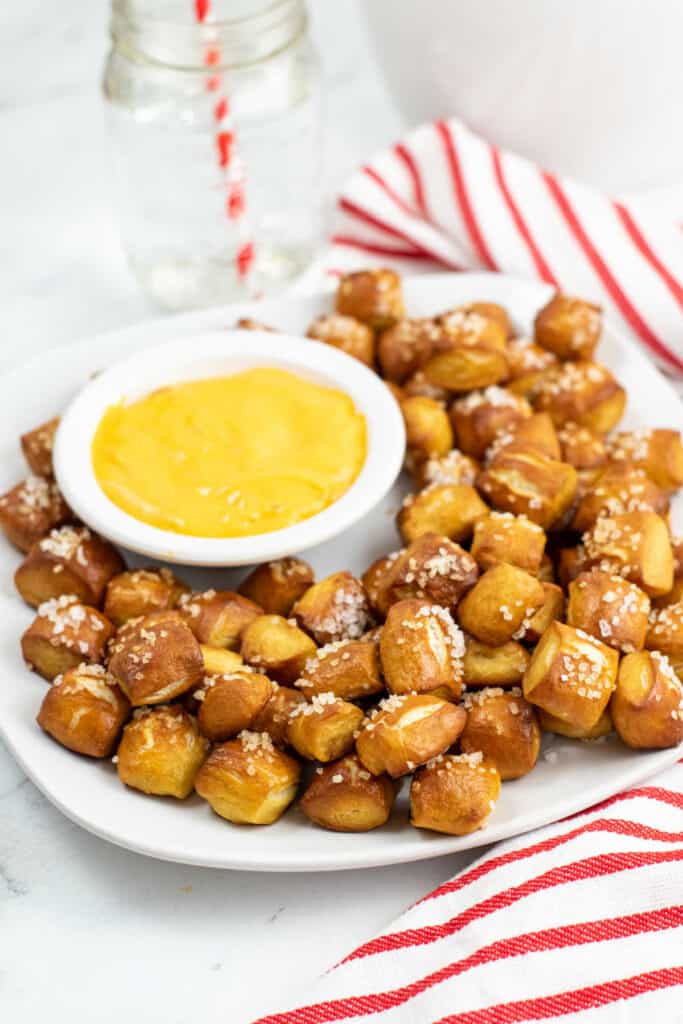 A plate full of soft pretzel bites on a white plate with a small white bowl of cheese dip. 
