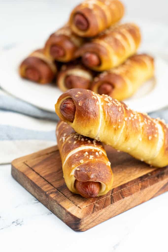Two pretzel dogs in the forefront with a plate full of pretzel dogs in the background. 