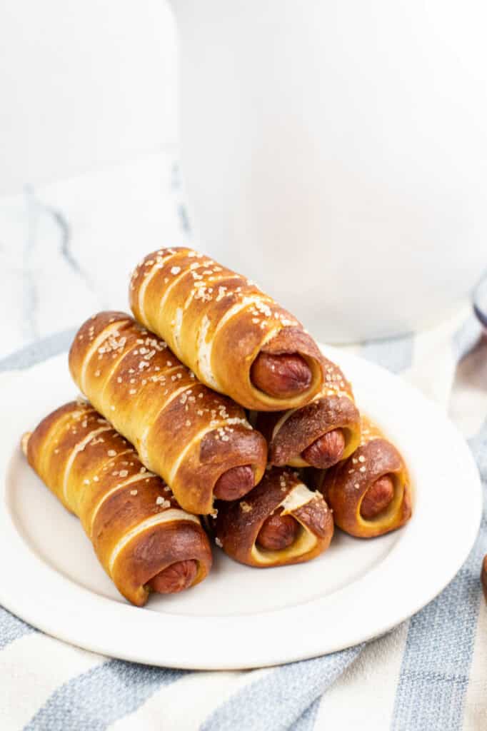 A white plate with a pile of pretzel dogs on it. 