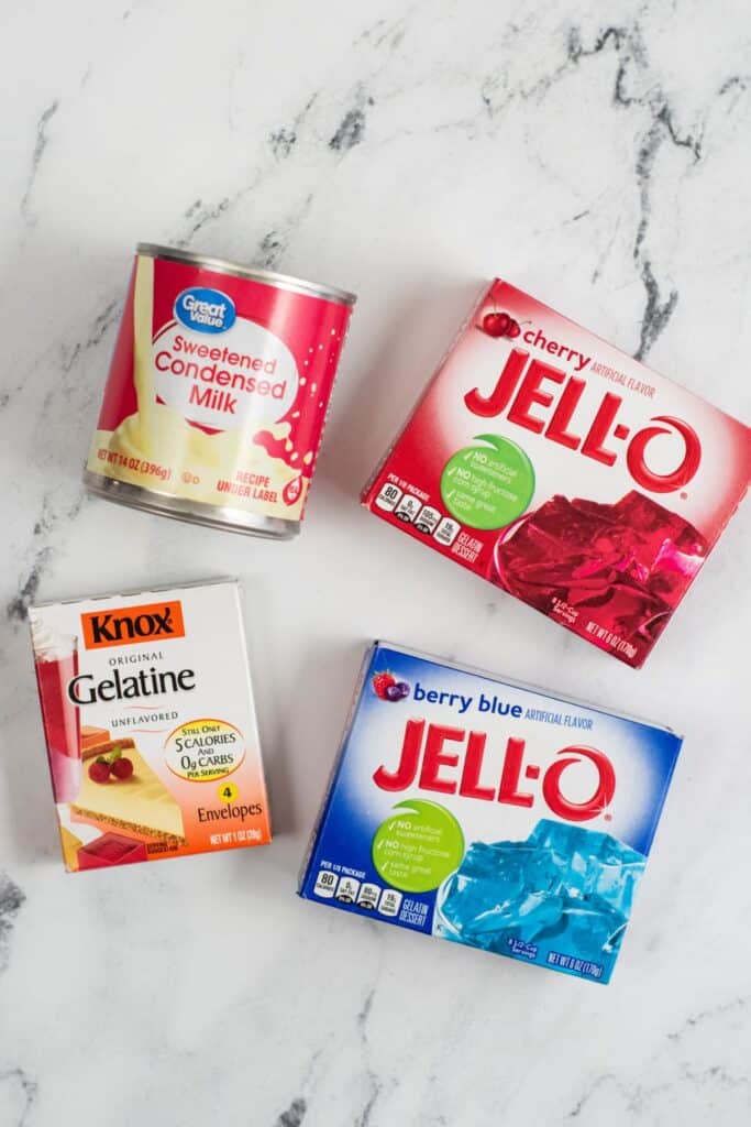 The ingredients for red white and blue layered Jell-o. Sweetened condensed milk, cherry Jell-o, berry blue Jell-o and unflavored gelatin. 