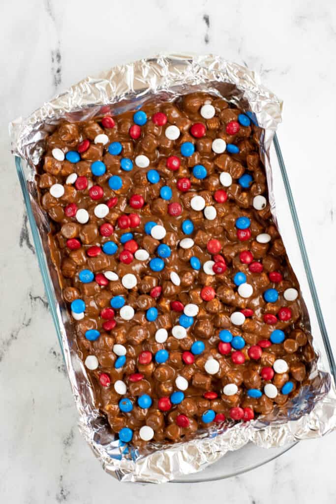 A baking pan lined with aluminum foil filled with a marshmallow and chocolate mixture topped with red white & blue M&M's 