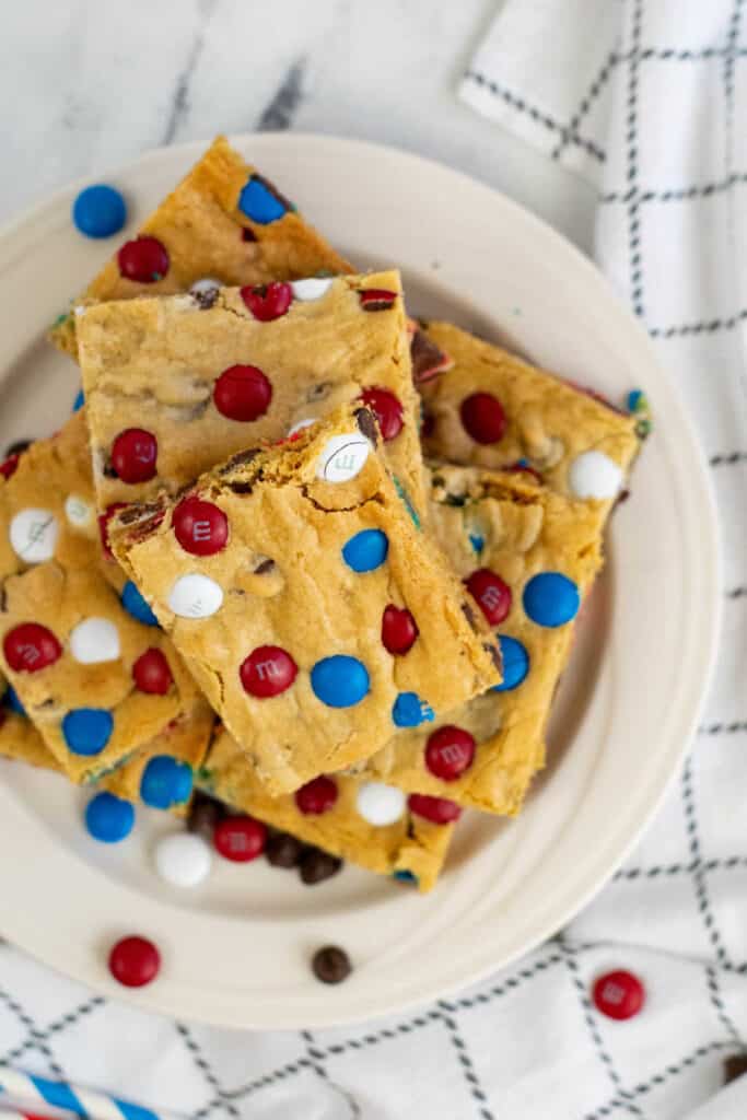 A pile of red white and blue M&M cookie bars on a white plate. 