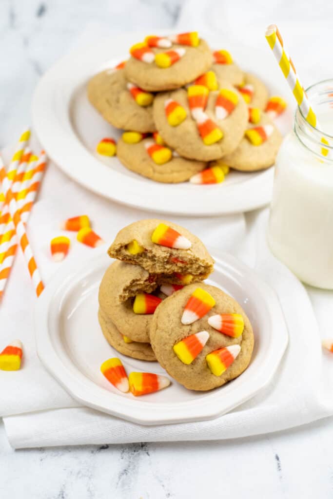a pile of candy corn cookies on a white plate with a mason jar full of milk in the background. 