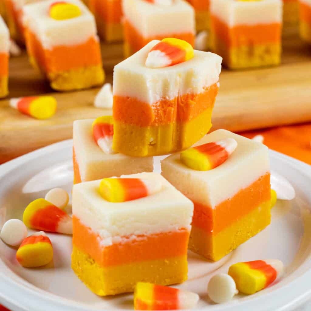four pieces of yellow, orange and white fudge stacked on a white plate. 