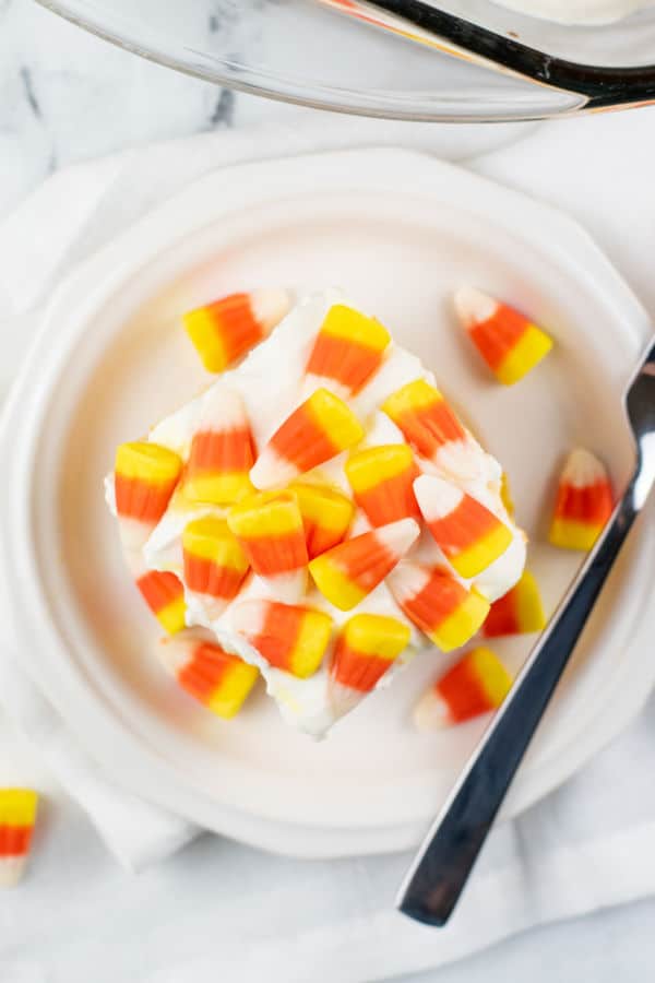 A small white plate with a piece of cake topped with candy corn on it. 