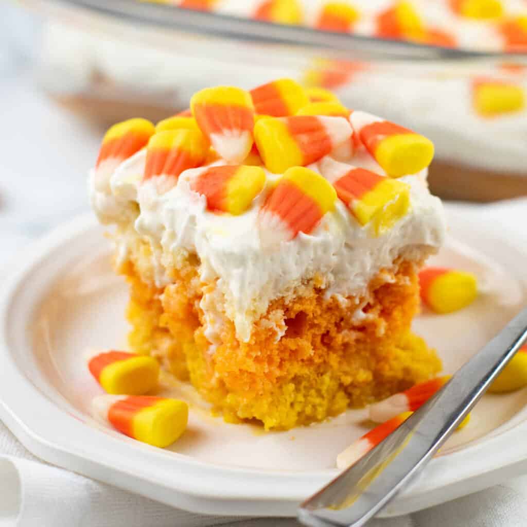 a piece of candy corn poke cake on a white plate. 