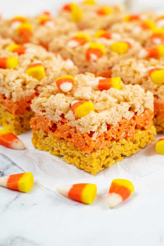 A close up of a candy corn rice krispie treats with yellow, orange and white layers topped with candy corn. 