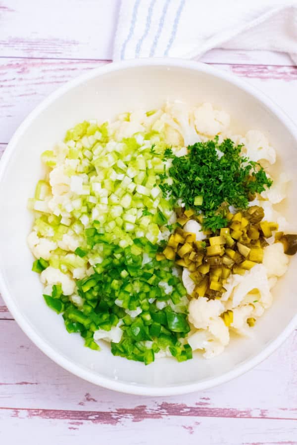 A large white bowl with cauliflower, chopped pickles, celery and green pepper in it. 