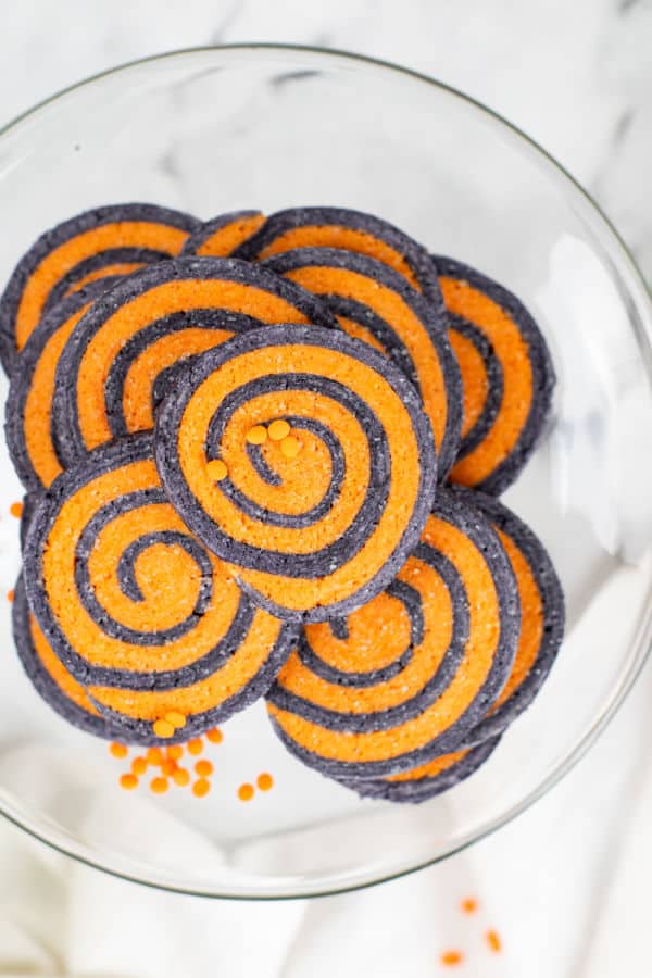 A pile of black and orange pinwheel cookies on a glass cake stand. 