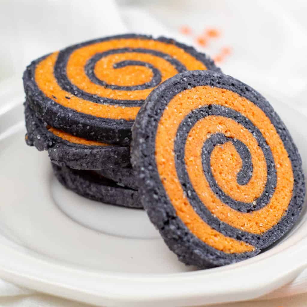 A stack of black and orange Halloween pinwheel cookies on a white plate. 