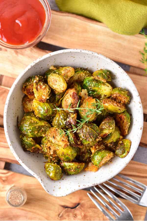 A white bowl full of roasted brussels sprouts on a wooden background. 