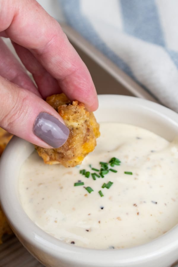 A hand dipping a sausage ball into a white dip garnished with fresh chives. 
