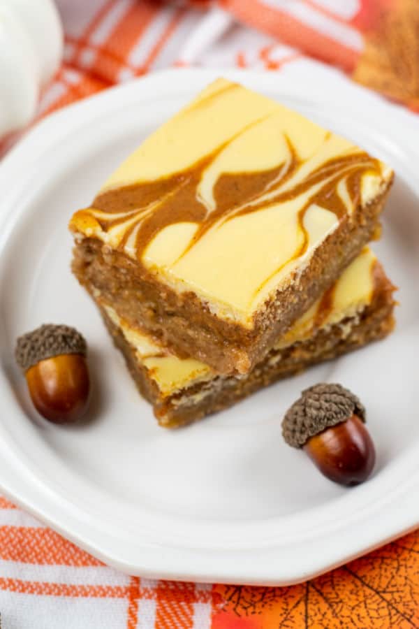 Two pumpkin cheesecake bars stacked on a white plate. 