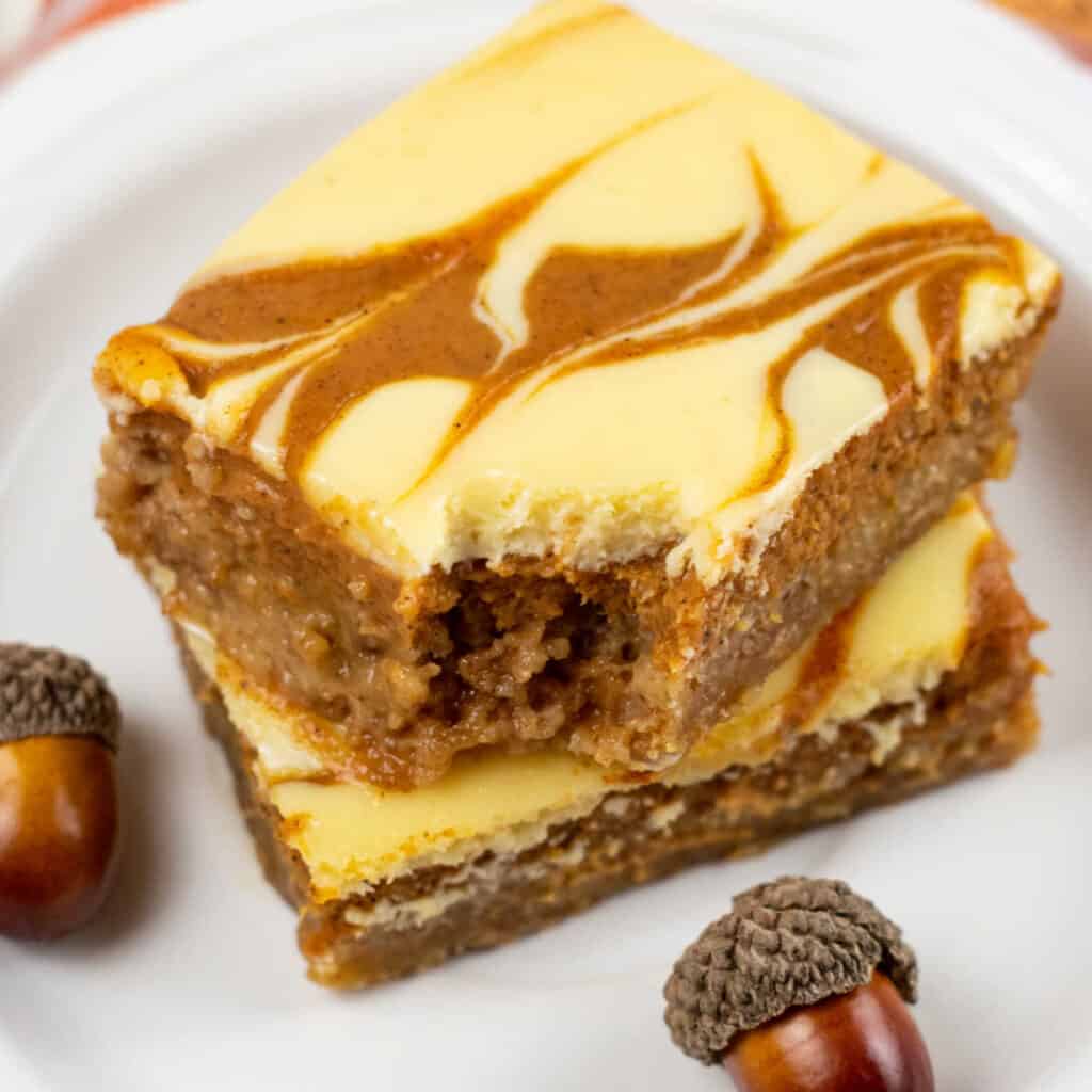 Two pumpkin cheesecake bars stacked on a plate. 